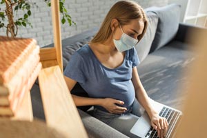 Pregnant lady wearing surgical mask looking at laptop