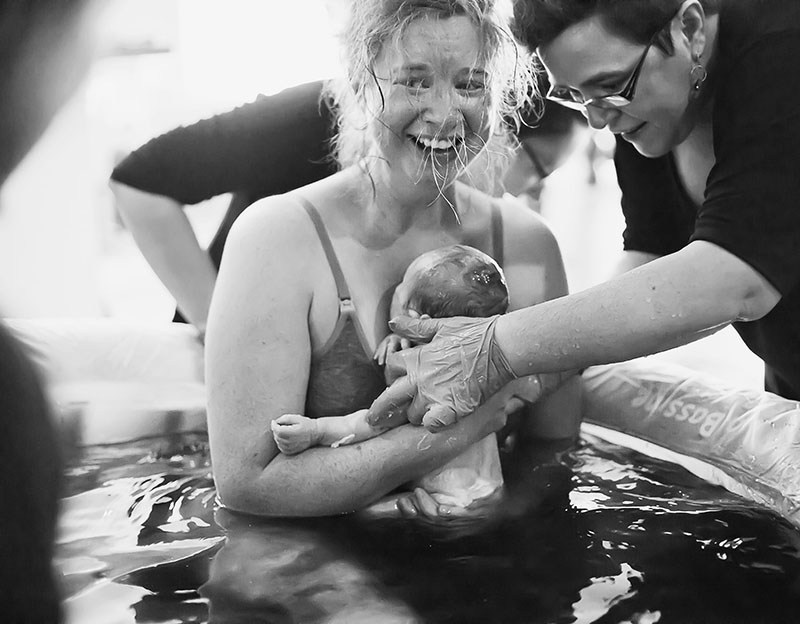 Woman in a birthing pool holding a new born baby